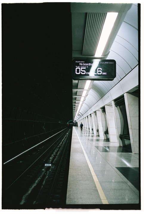 A man walks along a brightly lit subway platform next to dark train tracks.