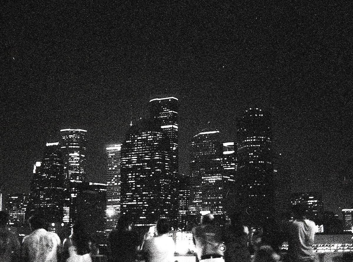 A group of people stand with their backs to the camera, looking at a city skyline at night.
