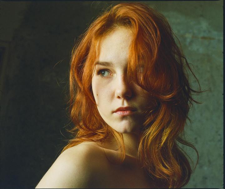 A woman with long red hair looks over her shoulder.