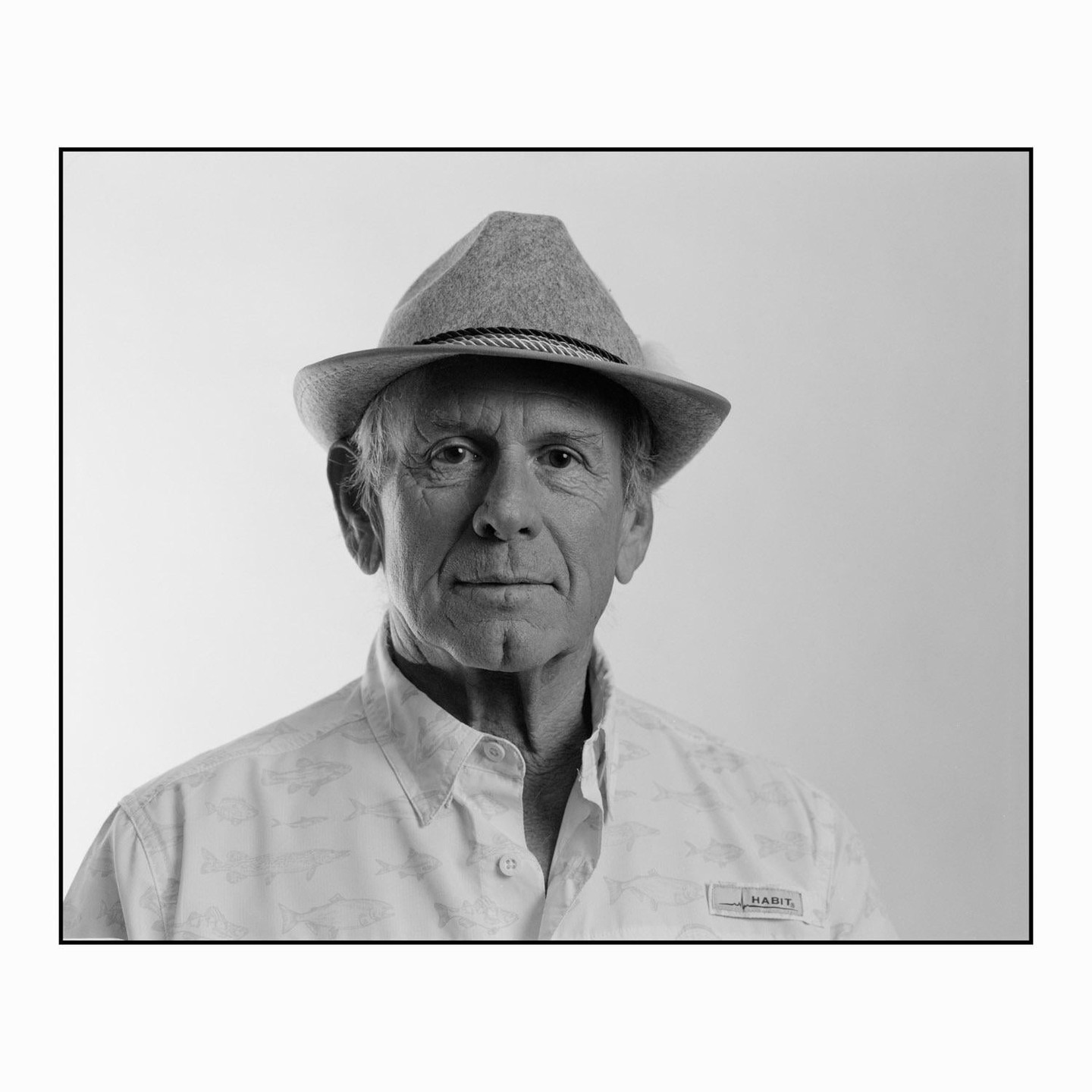 A man wearing a hat and a patterned shirt looks directly at the viewer.