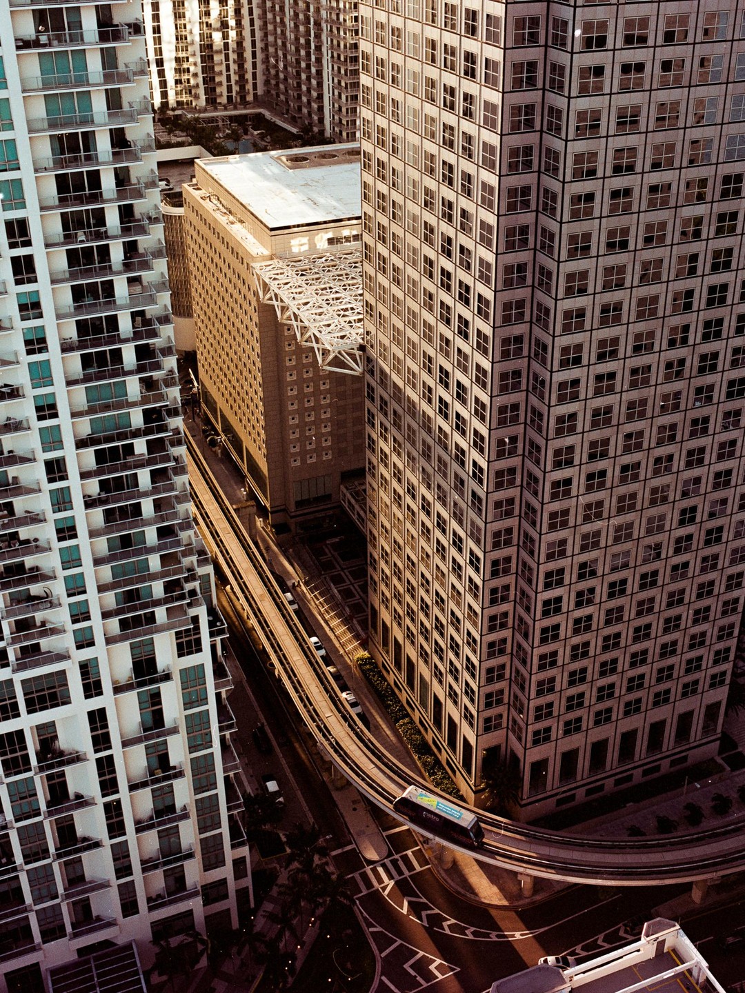 An elevated view shows a monorail train on a curved track between tall buildings in a city.