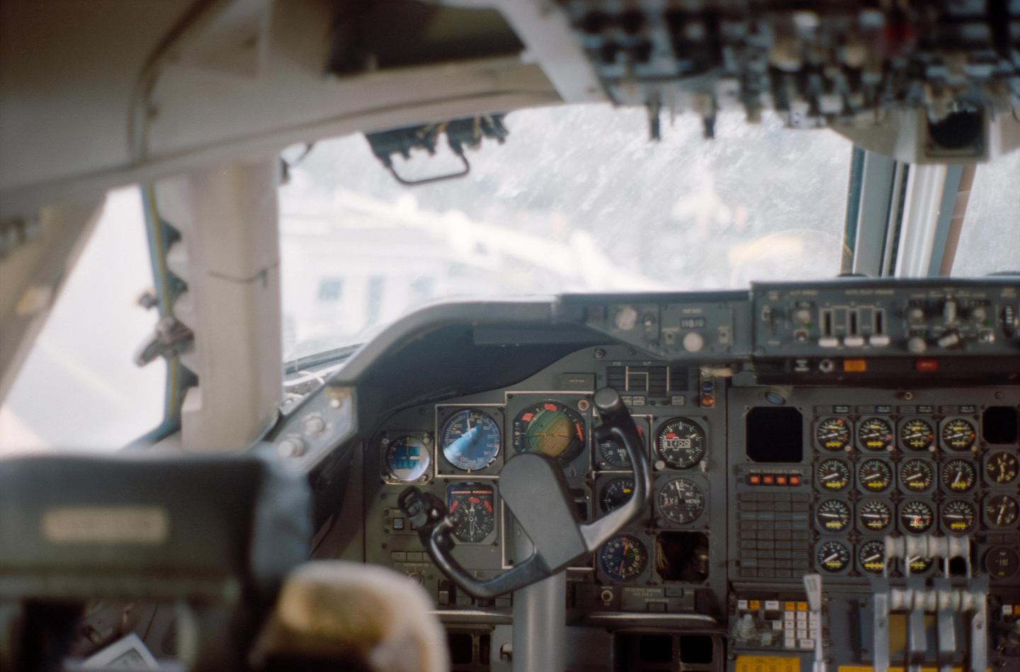 The cockpit of an airplane is visible, showing the steering yoke and numerous gauges and controls.