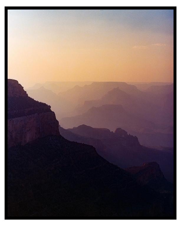 A vast canyon landscape is visible at dusk, with layers of mountains fading into the distance under a colorful sky.