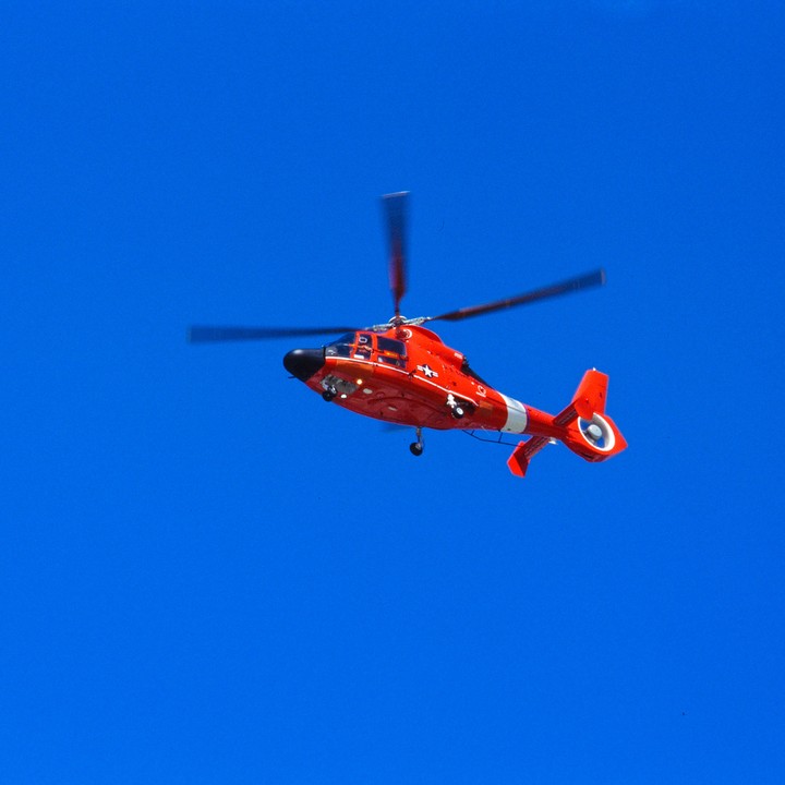 A red and white helicopter flies against a bright blue sky.
