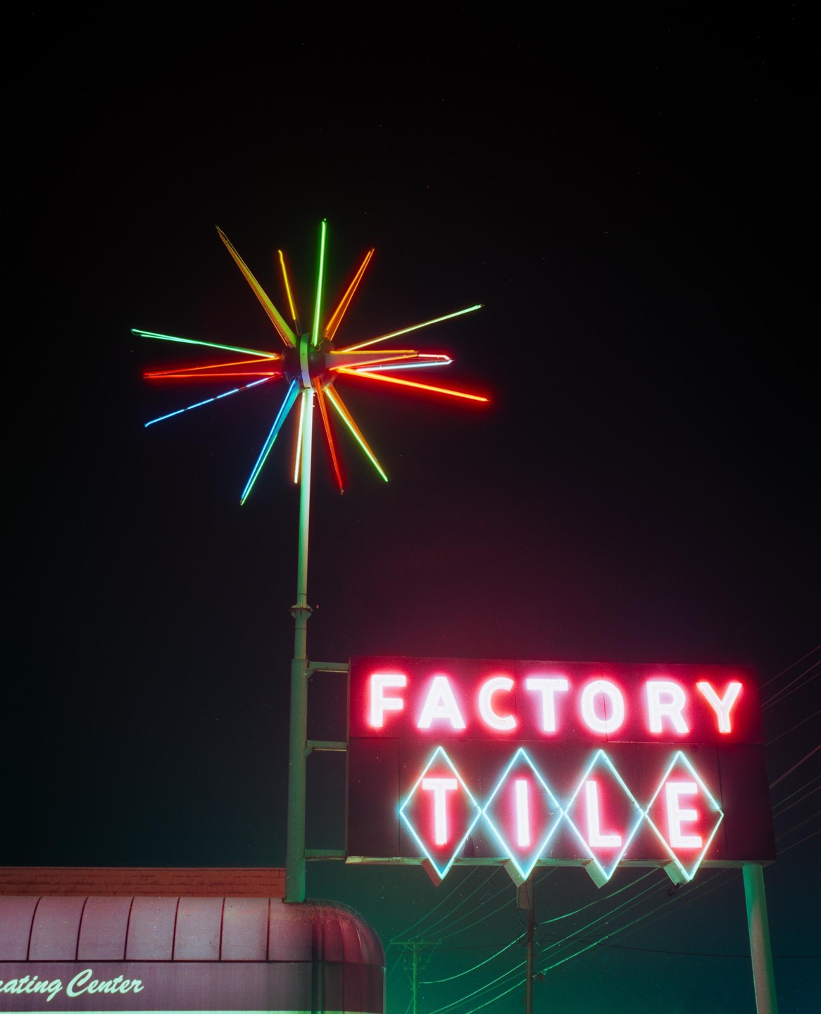 A neon sign for "Factory Tile" with a colorful starburst decoration is illuminated against a dark night sky.