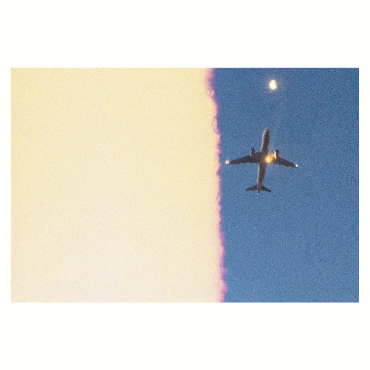 An airplane flies across a bright blue sky with a bright light in the distance.