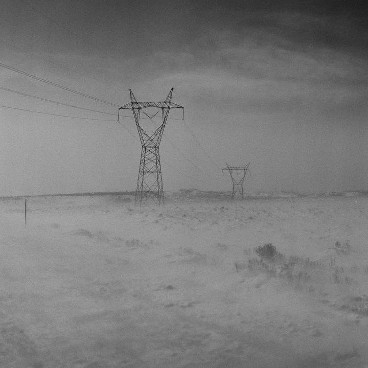 Two electricity pylons stand in a hazy, snow-covered landscape under a dark sky.
