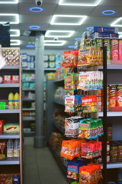 A narrow aisle in a convenience store is filled with shelves of snacks and drinks.
