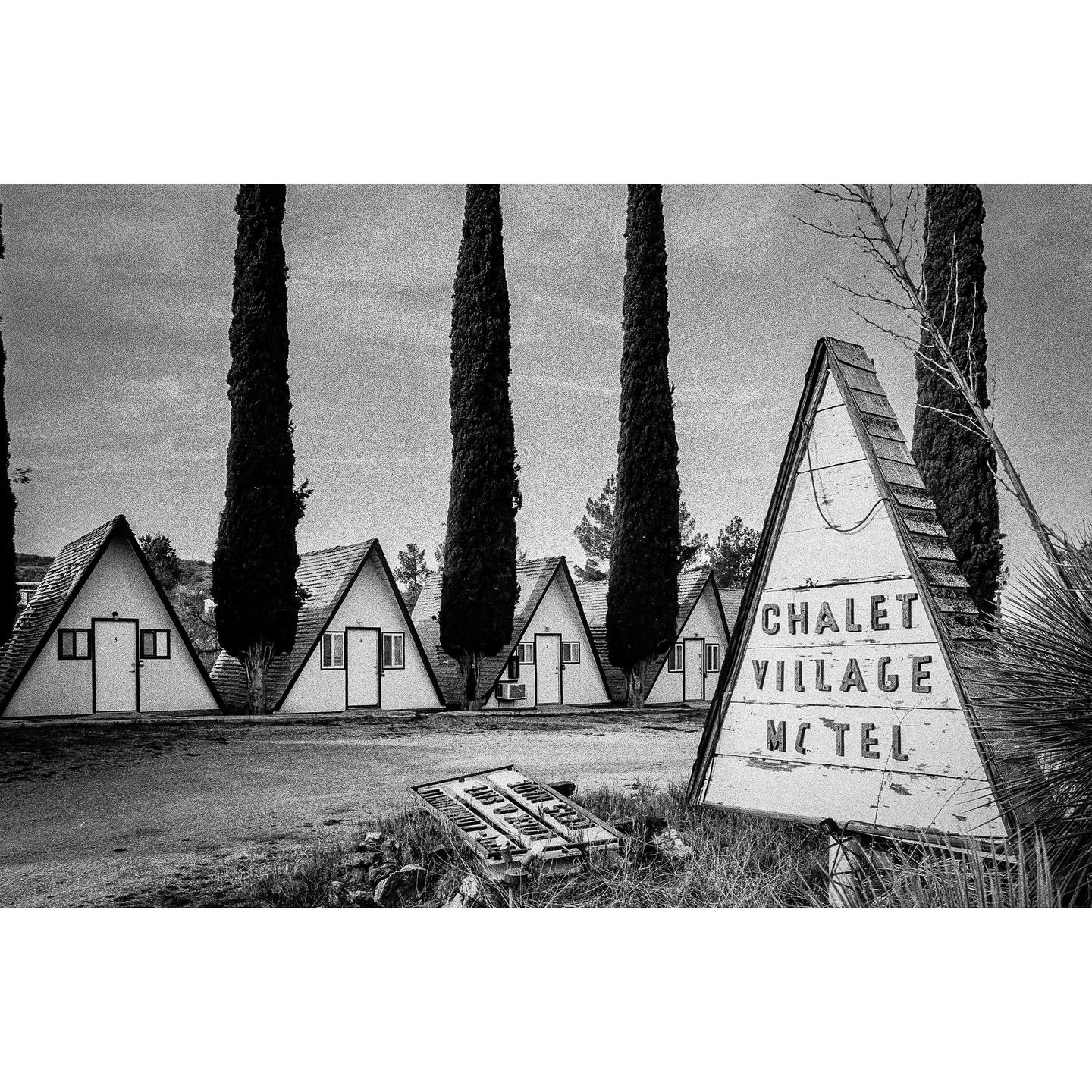 A row of A-frame chalets stands behind a triangular "Chalet Village Motel" sign.