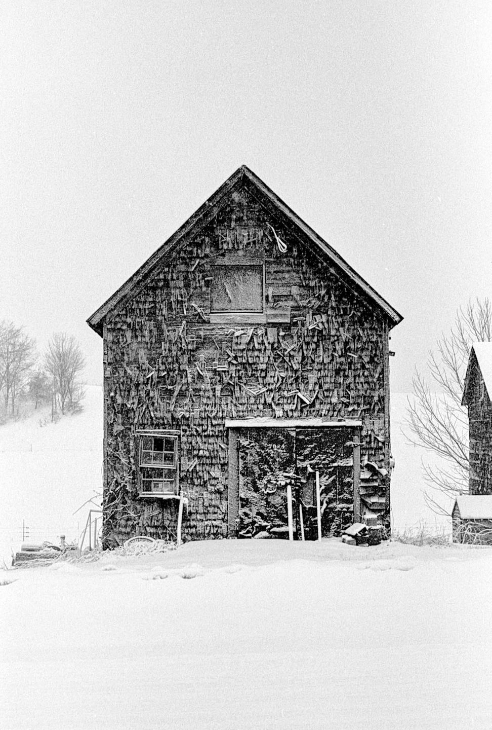 An old wooden barn with peeling paint stands in a snowy landscape.