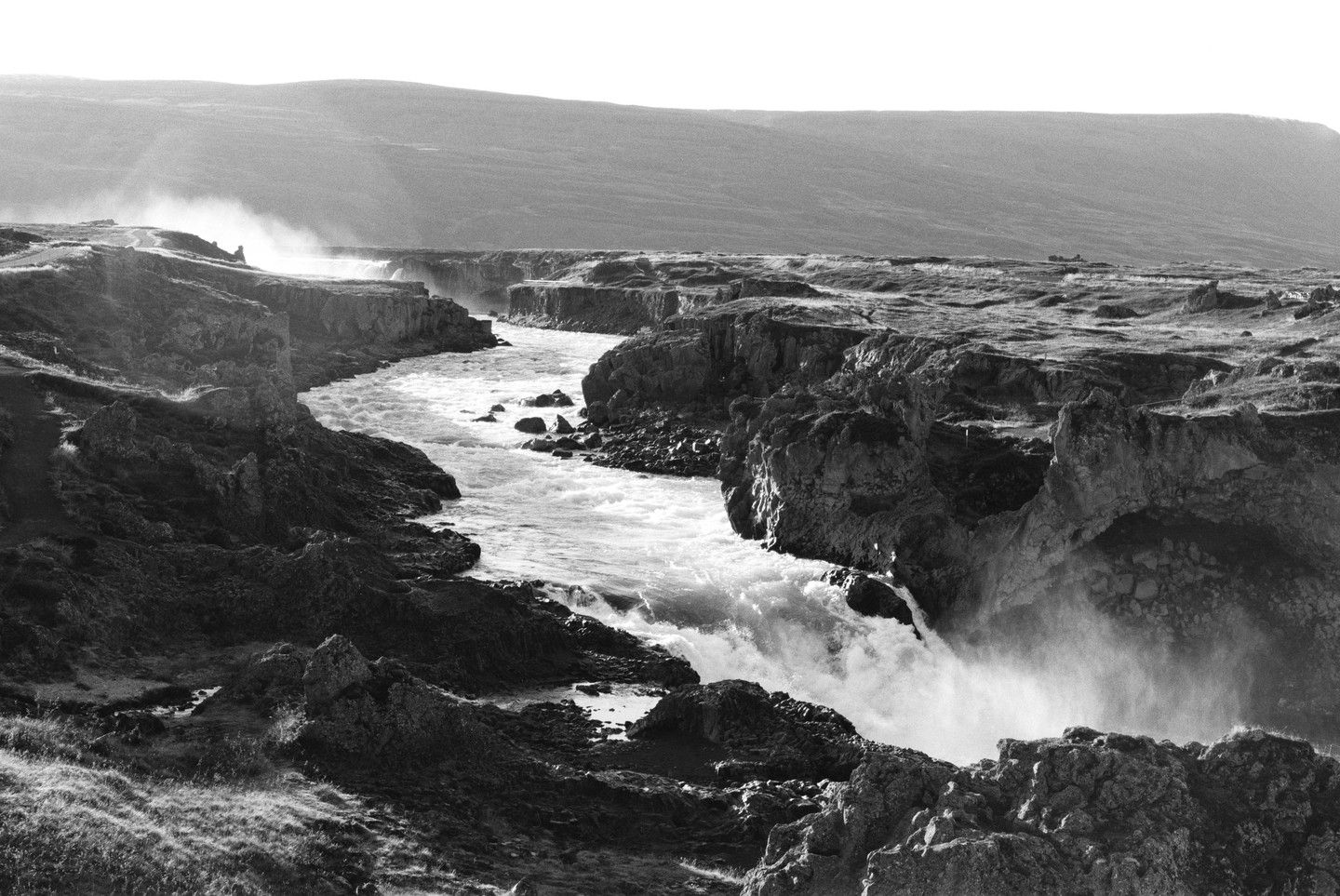 A river flows through a rocky canyon with a waterfall and mist rising from the water.