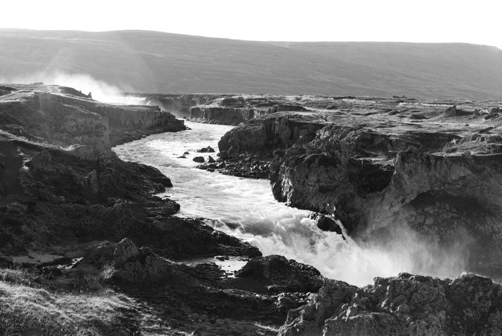 A river flows through a rocky canyon with a waterfall and mist rising from the water.