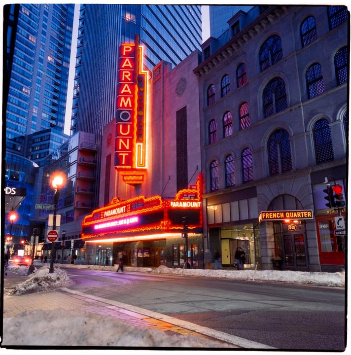 A street scene at dusk shows the Paramount Theatre with its neon sign illuminated, and snow on the ground.