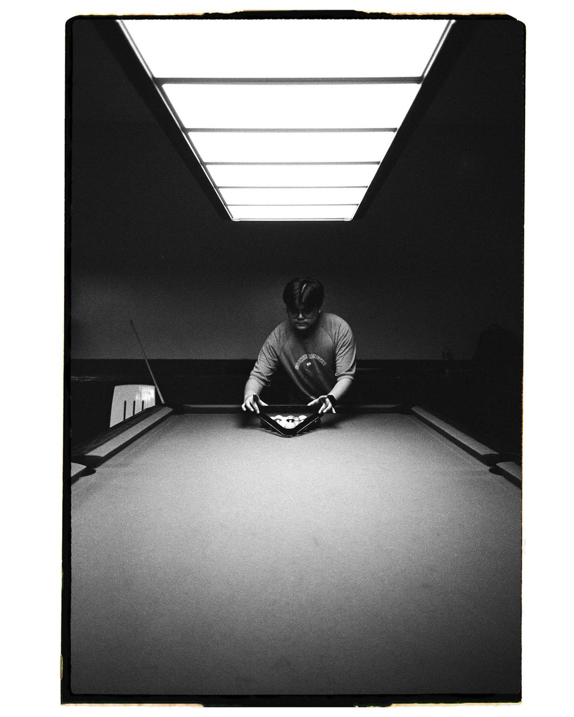 A man racks billiard balls on a pool table under a bright overhead light.