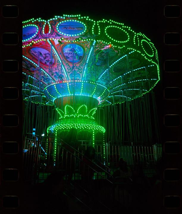 A brightly lit swing ride glows green and blue at night.