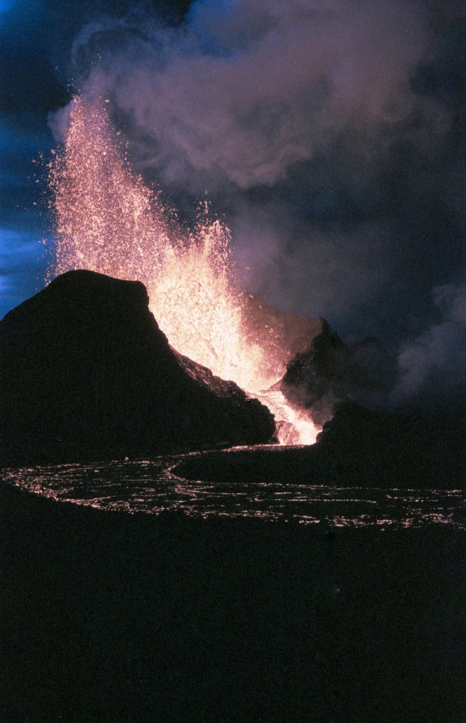 A volcano erupts at night, spewing lava and smoke into the dark sky.