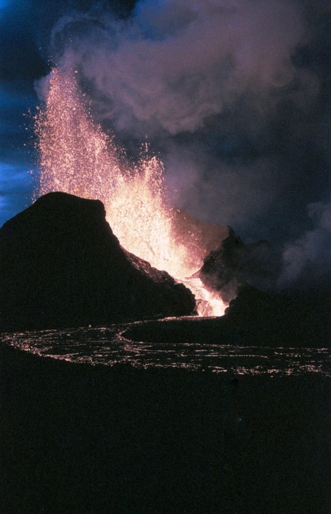 A volcano erupts at night, spewing lava and smoke into the dark sky.