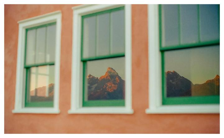 Three windows with green frames reflect a mountain range under a sunrise sky.