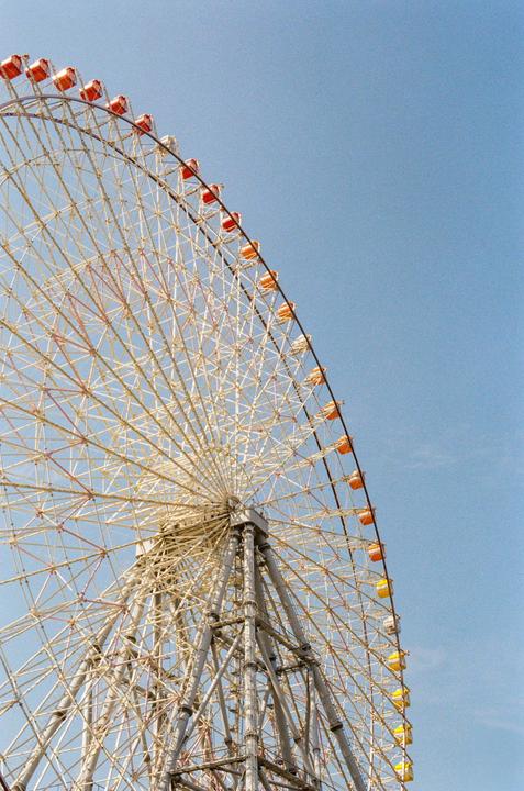 A large Ferris wheel with colorful gondolas is set against a clear blue sky.