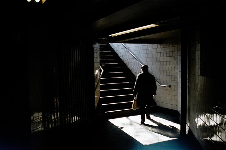 A man walks up a subway staircase with light and shadow creating a dramatic effect.