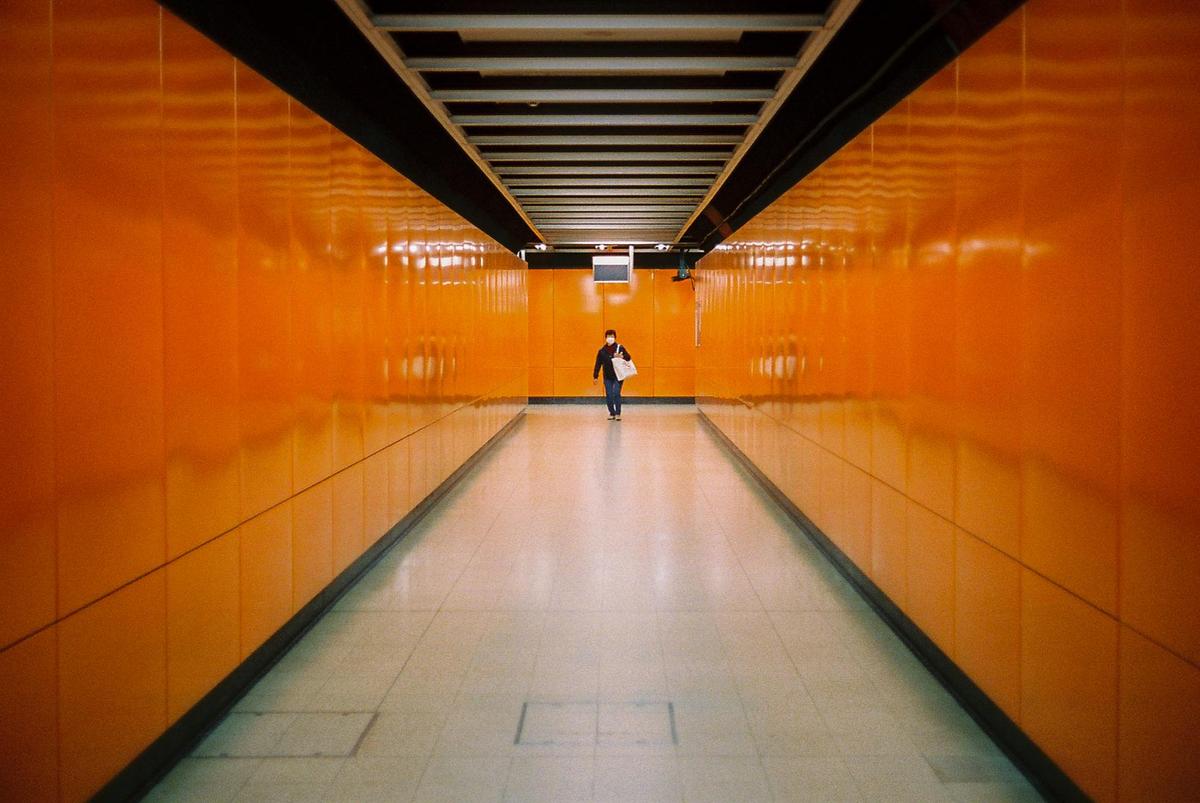 A person walks down a long, narrow, orange-walled corridor.