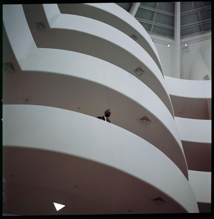A man in a suit and face mask stands on a balcony inside the Guggenheim Museum.