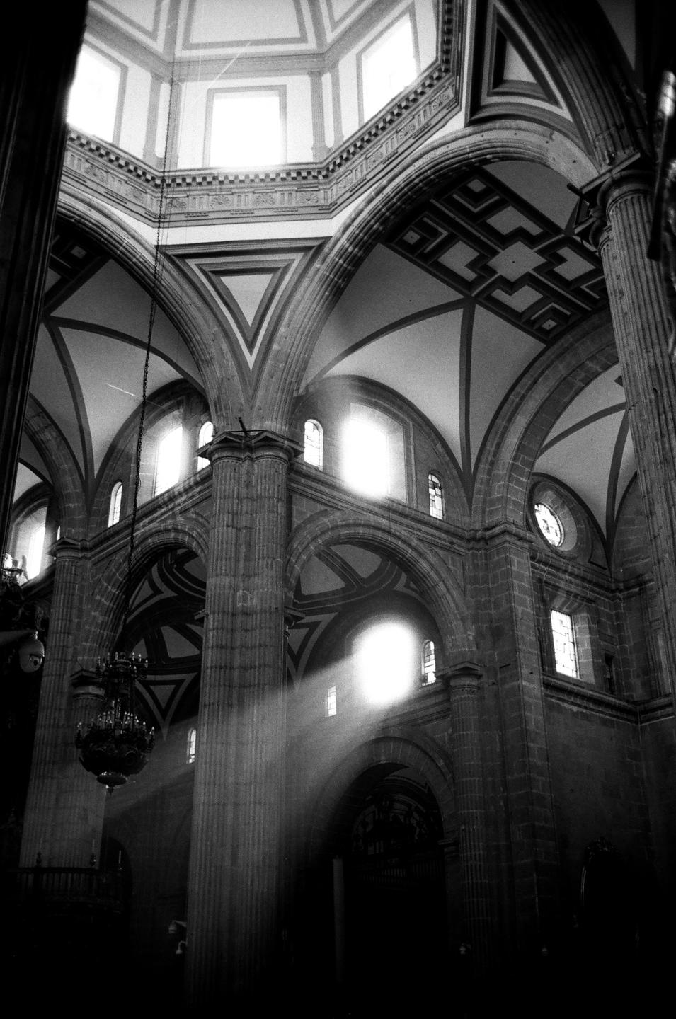 Sunlight streams through a window into a large, ornate church interior with high arched ceilings and columns.