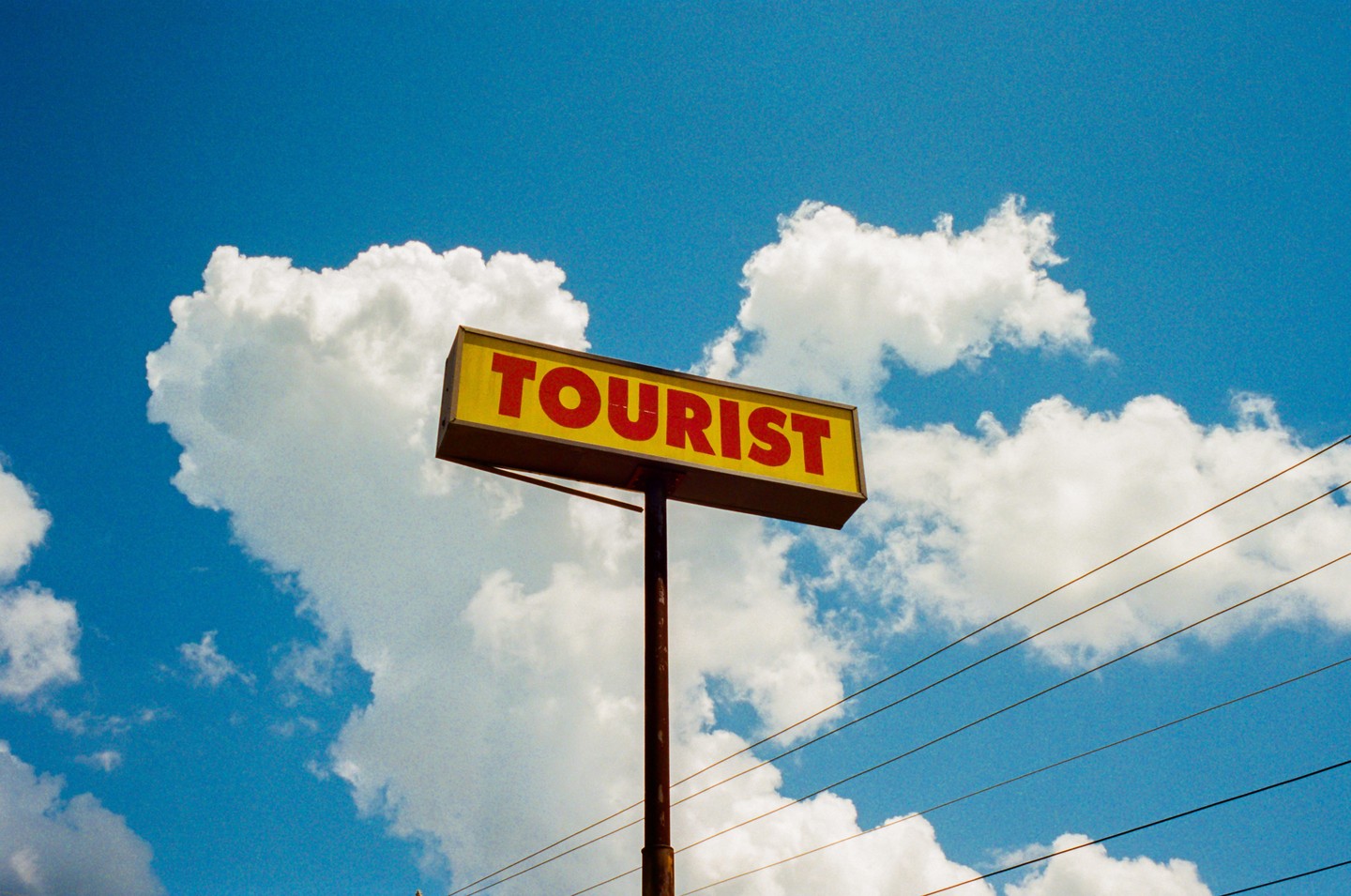 A yellow sign with the word "TOURIST" in red letters stands against a bright blue sky with white clouds.