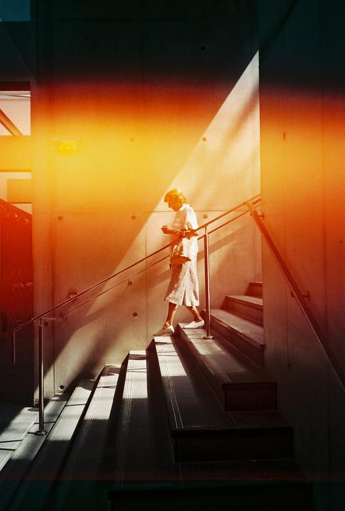 A woman walks down a concrete staircase with a handrail, illuminated by a strong diagonal beam of light.