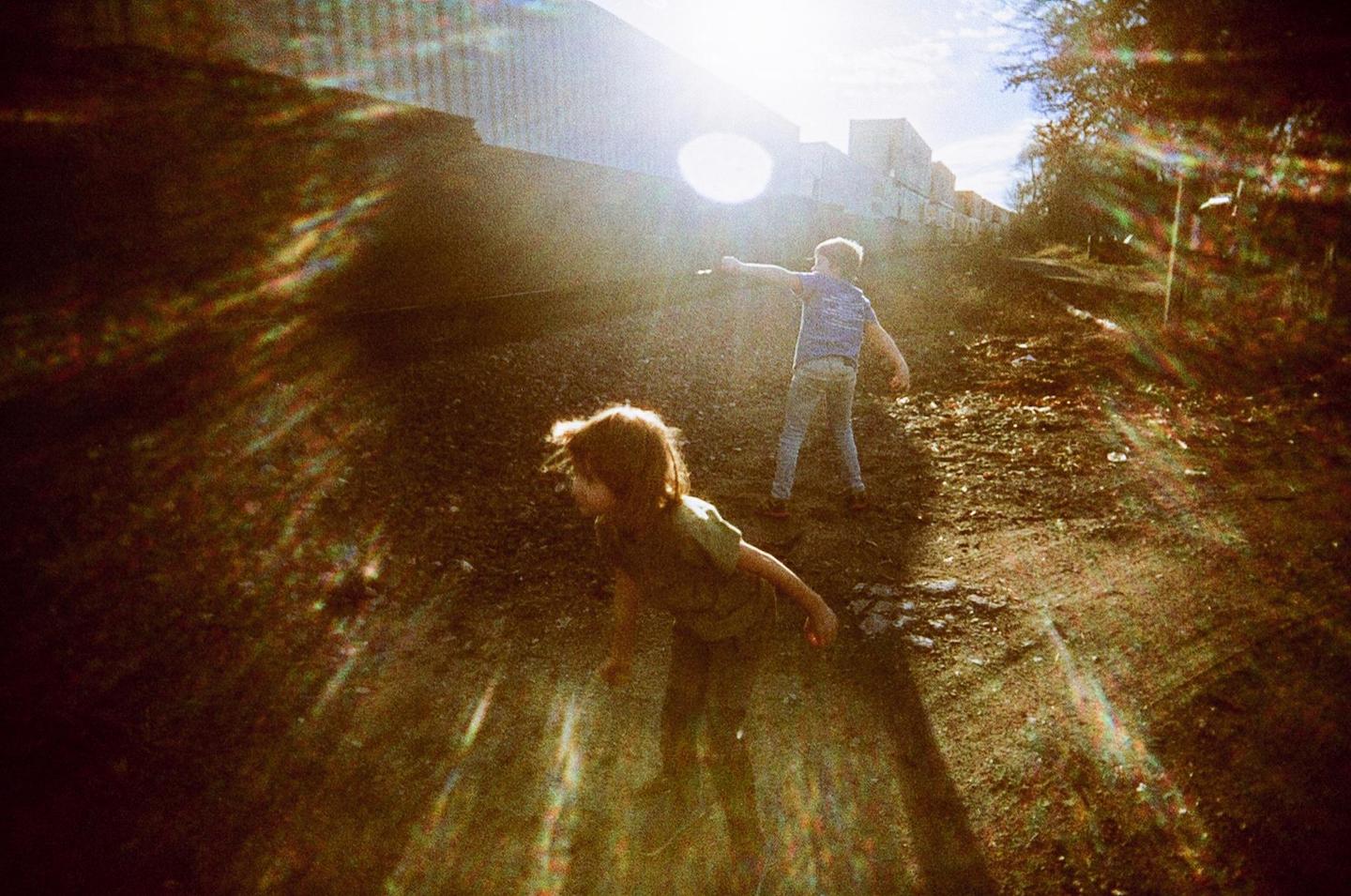 Two children are playing on a dirt path with bright sunlight and lens flare.