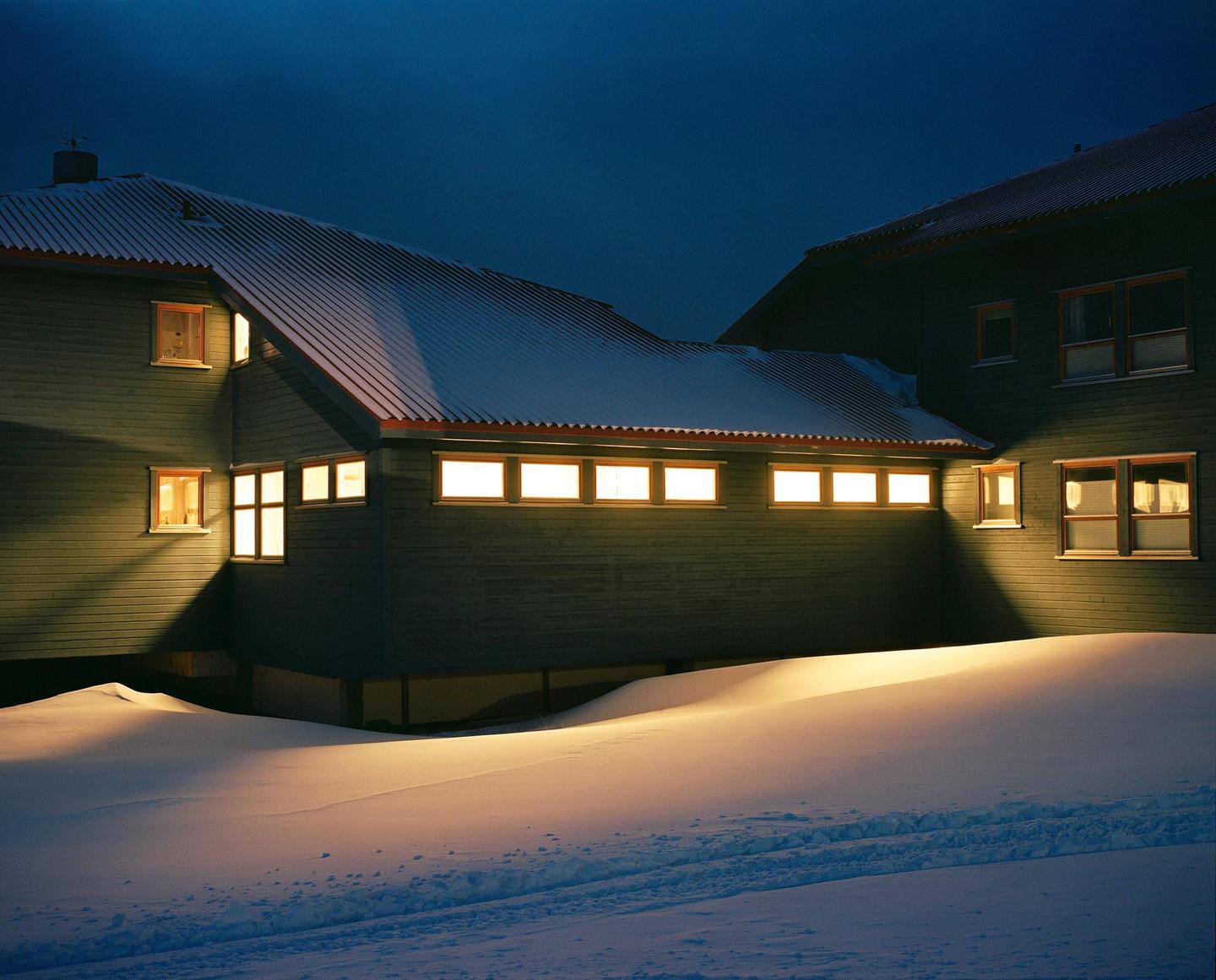 Two buildings with illuminated windows are surrounded by snow at night.