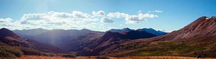 A panoramic landscape shows a valley with mountains and a bright sky with clouds.
