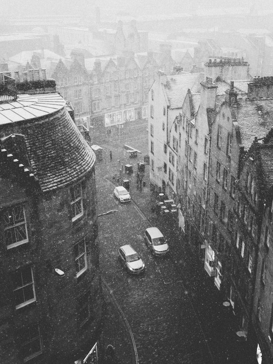 A high-angle view shows a street in Edinburgh with cars and buildings covered in snow.