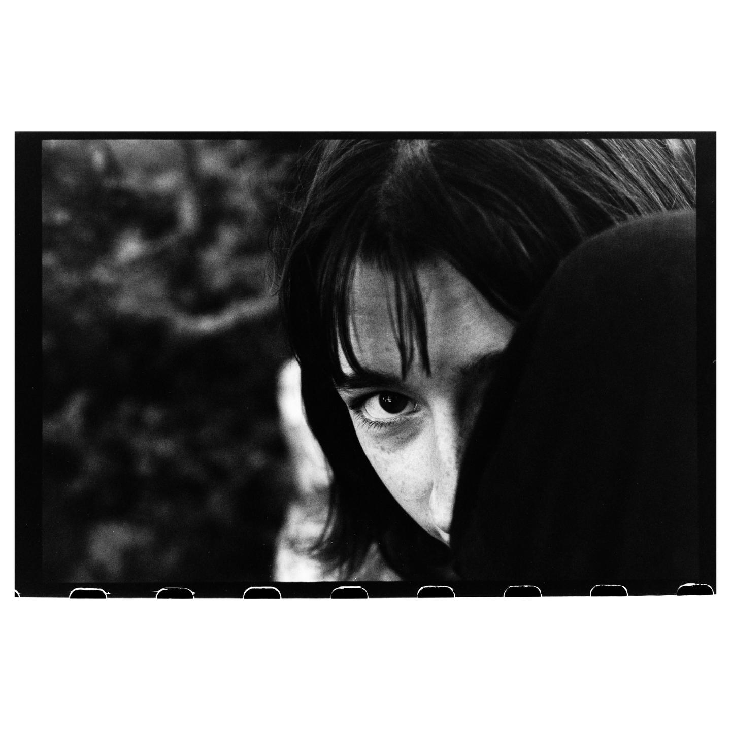 A woman with bangs and freckles looks directly at the viewer, with part of her face obscured by shadow.