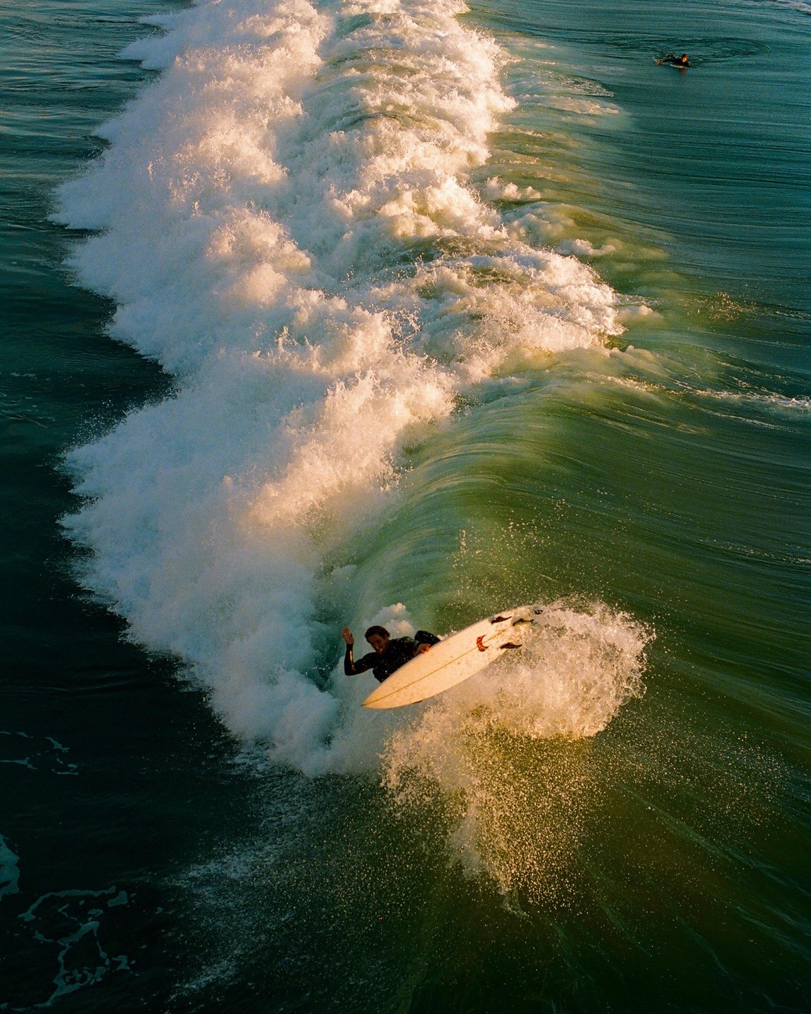 A surfer rides a large wave, with another surfer visible in the distance.