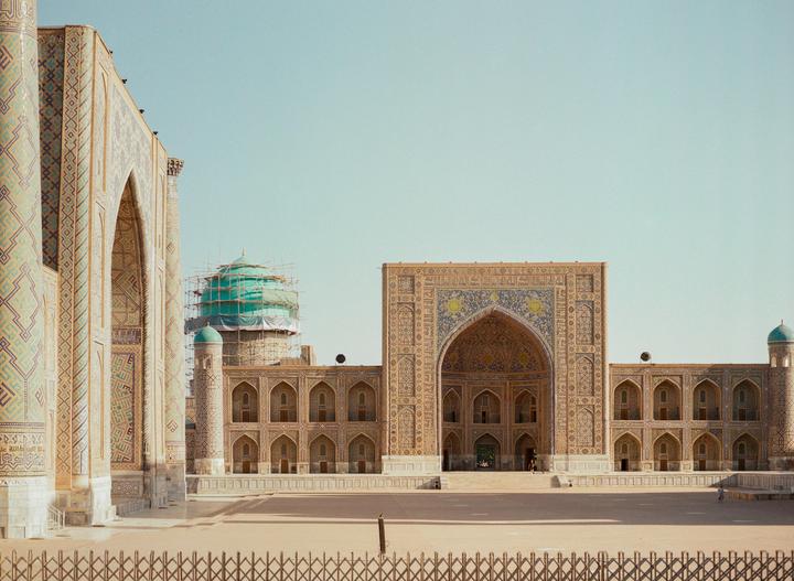 A large, ornate building with a domed roof under construction stands next to another ornate building with a large arched entrance.