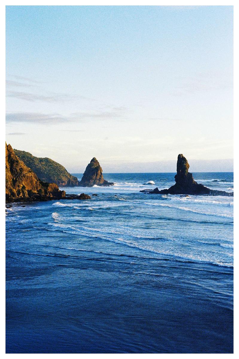 Waves crash against a rocky coastline with two large sea stacks rising from the water.
