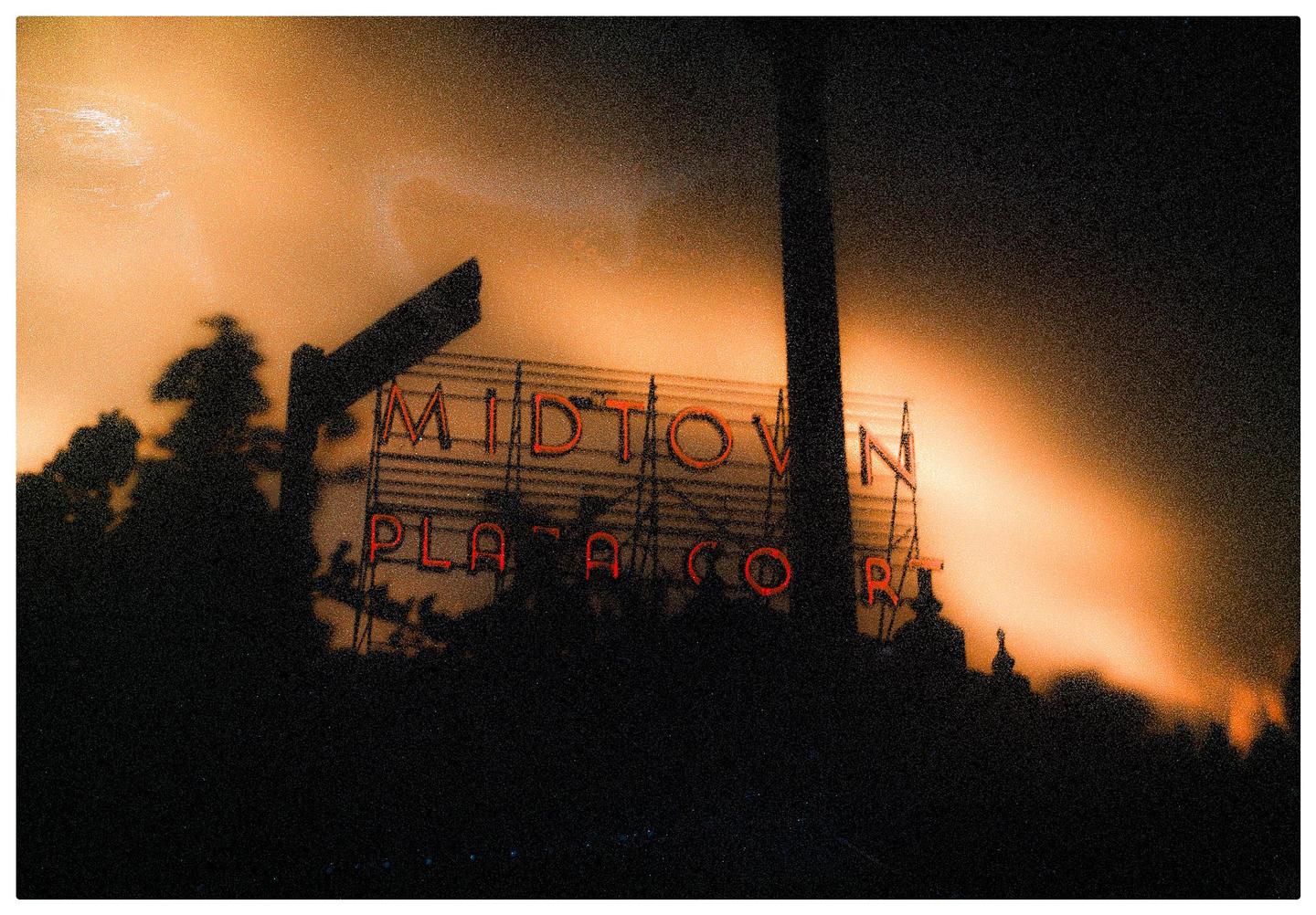 A neon sign for Midtown Plaza is visible against an orange sky at night.