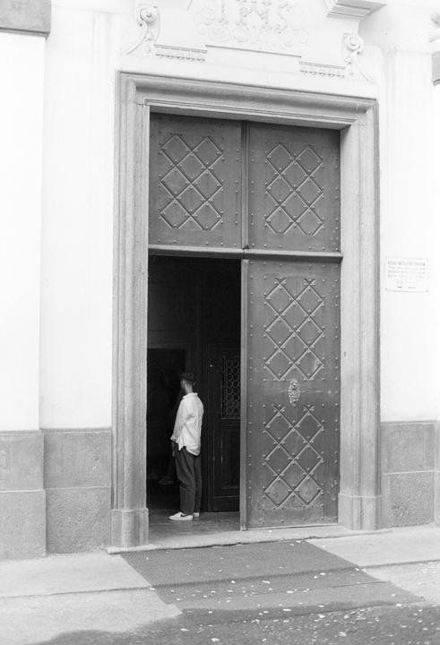 A man stands in the doorway of a large building with ornate doors.