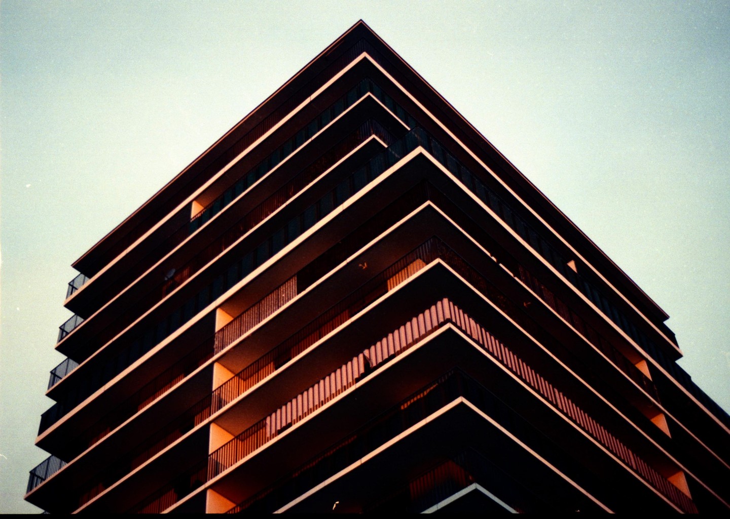 A modern building with balconies is photographed from a low angle against a clear sky.