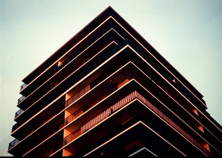 A modern building with balconies is photographed from a low angle against a clear sky.