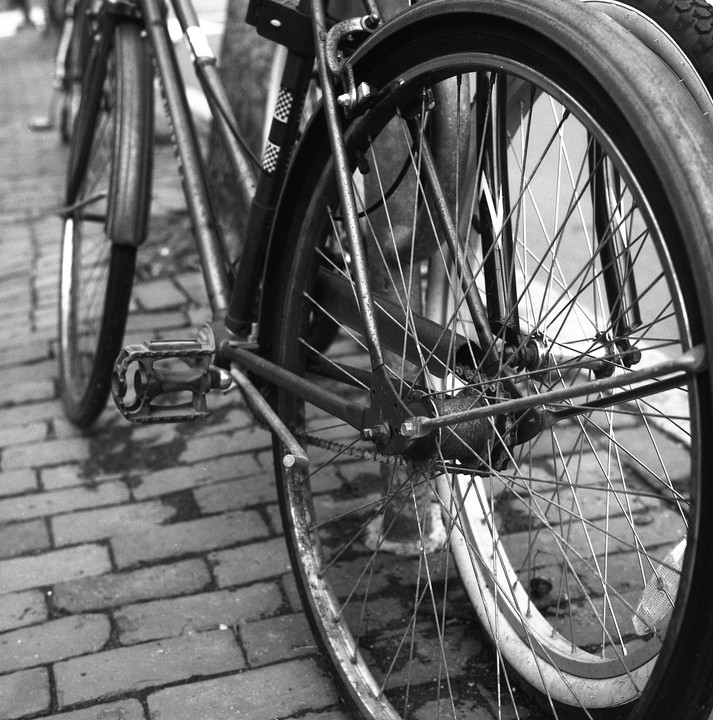 Two bicycles are parked on a brick street, with one bicycle wheel in the foreground.