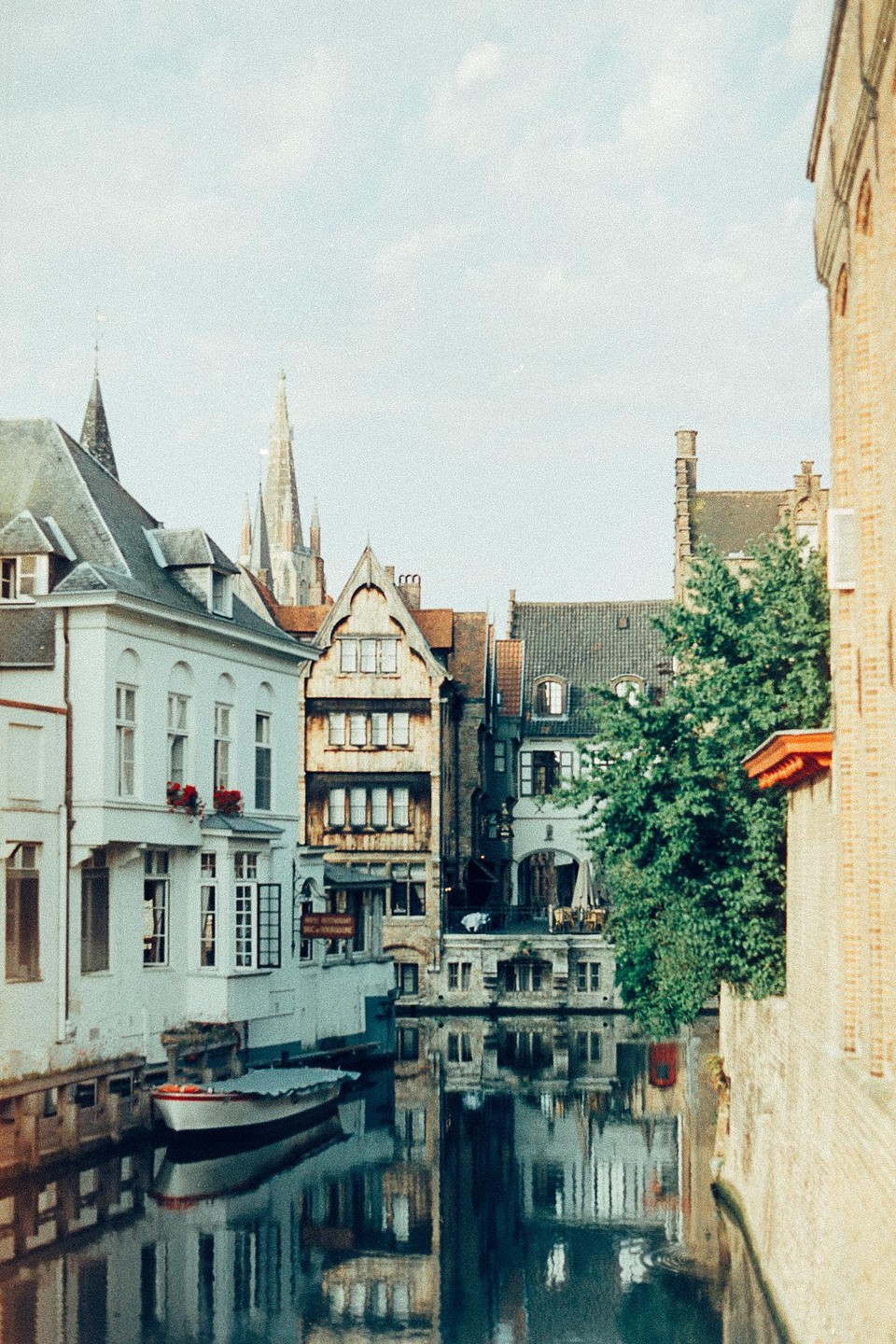 A canal with a boat is surrounded by buildings with a church spire in the background.
