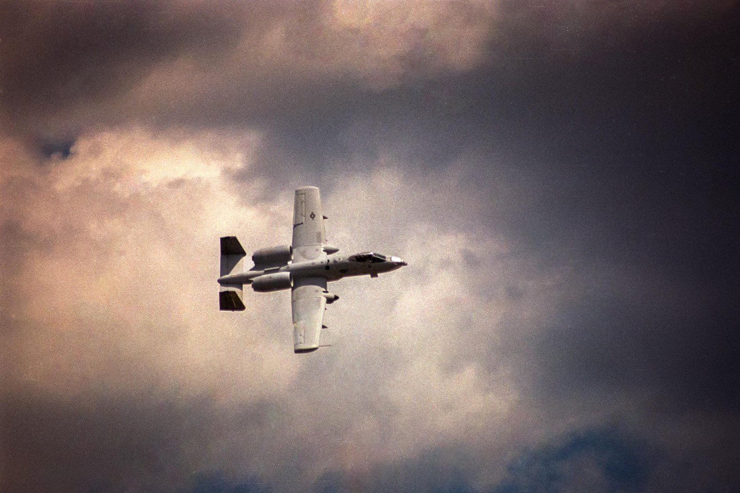 A military aircraft flies through a cloudy sky.