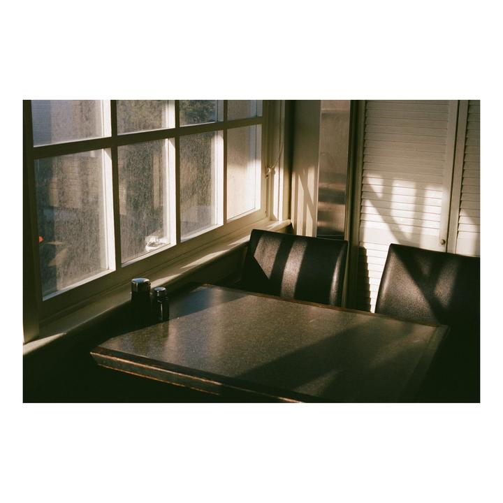 Sunlight streams through a window onto a diner table with two chairs and salt and pepper shakers.