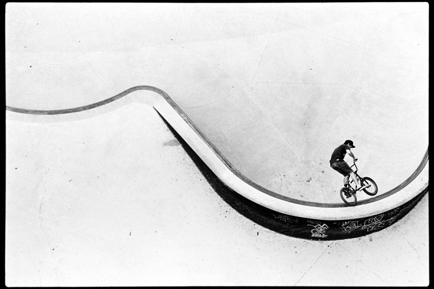 A man rides a BMX bike in a skatepark bowl.