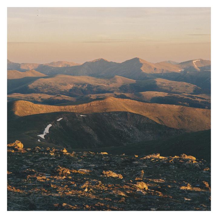 The sun illuminates a rocky mountain landscape with patches of snow.