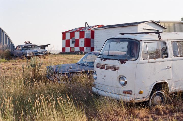 Three old vehicles are parked in a grassy field next to a red and white checkered building.