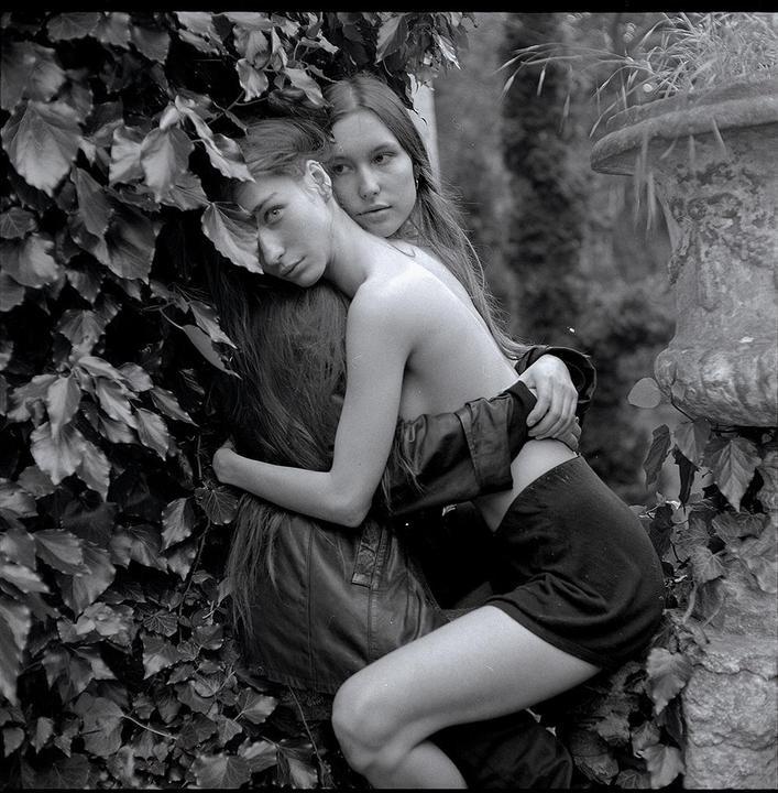 Two women are embracing each other while surrounded by ivy and a stone planter.