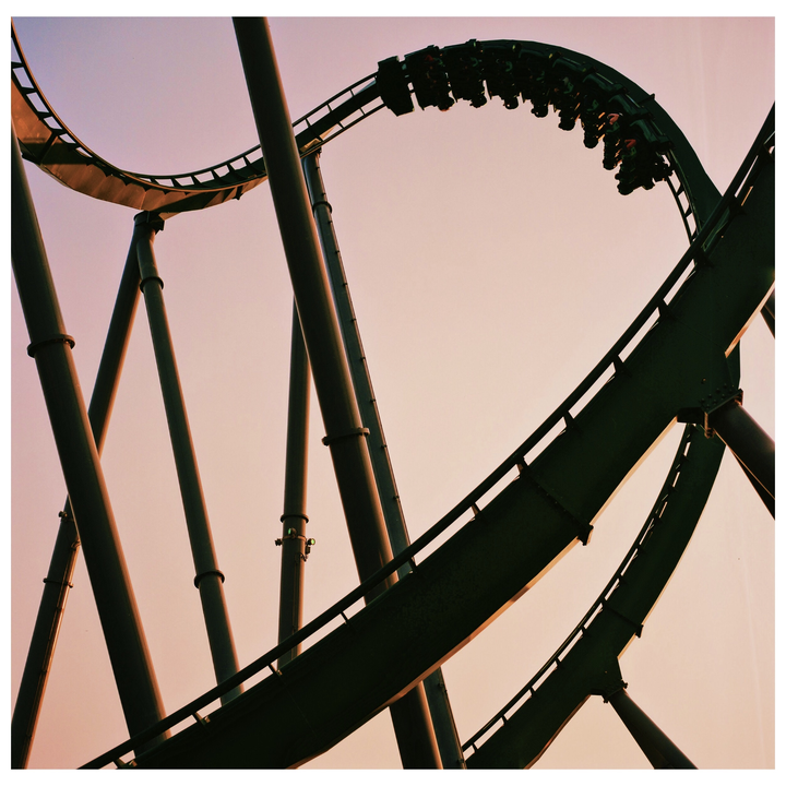 A roller coaster with people riding in it curves against a pale sky.
